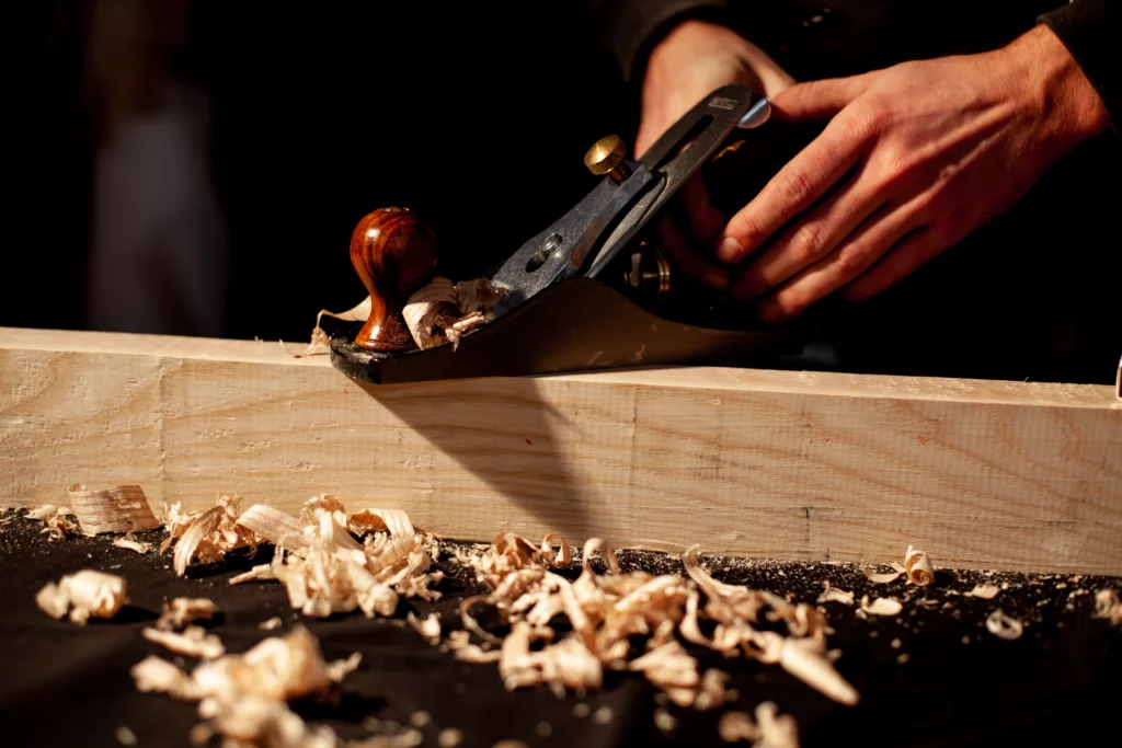 mains qui utilisent un rabot à bois manuel sur une pièce de bois et copeaux