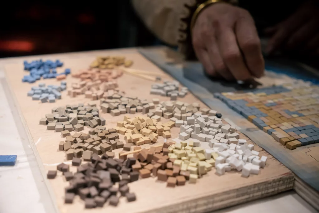 travail de mosaïque en cours, tesselles bleu clair, bleu foncé, beige, jaune, marron, orange, blanche disposées sur la pièce en fabrication