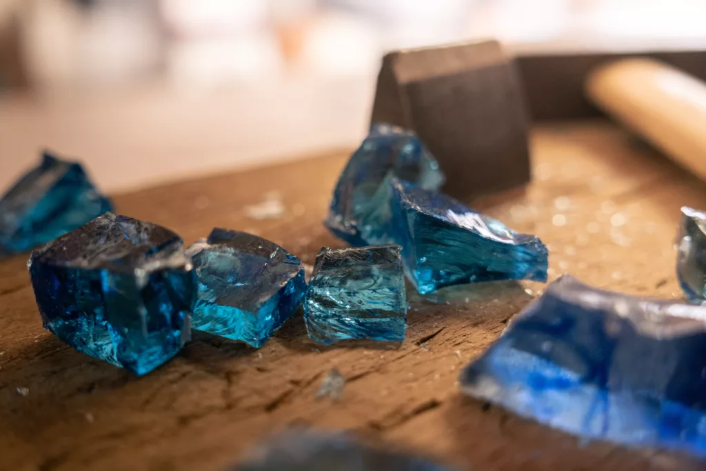 tesselles bleues roi, en verre translucide en cours de coupe sur un plan de travail, avec un marteau