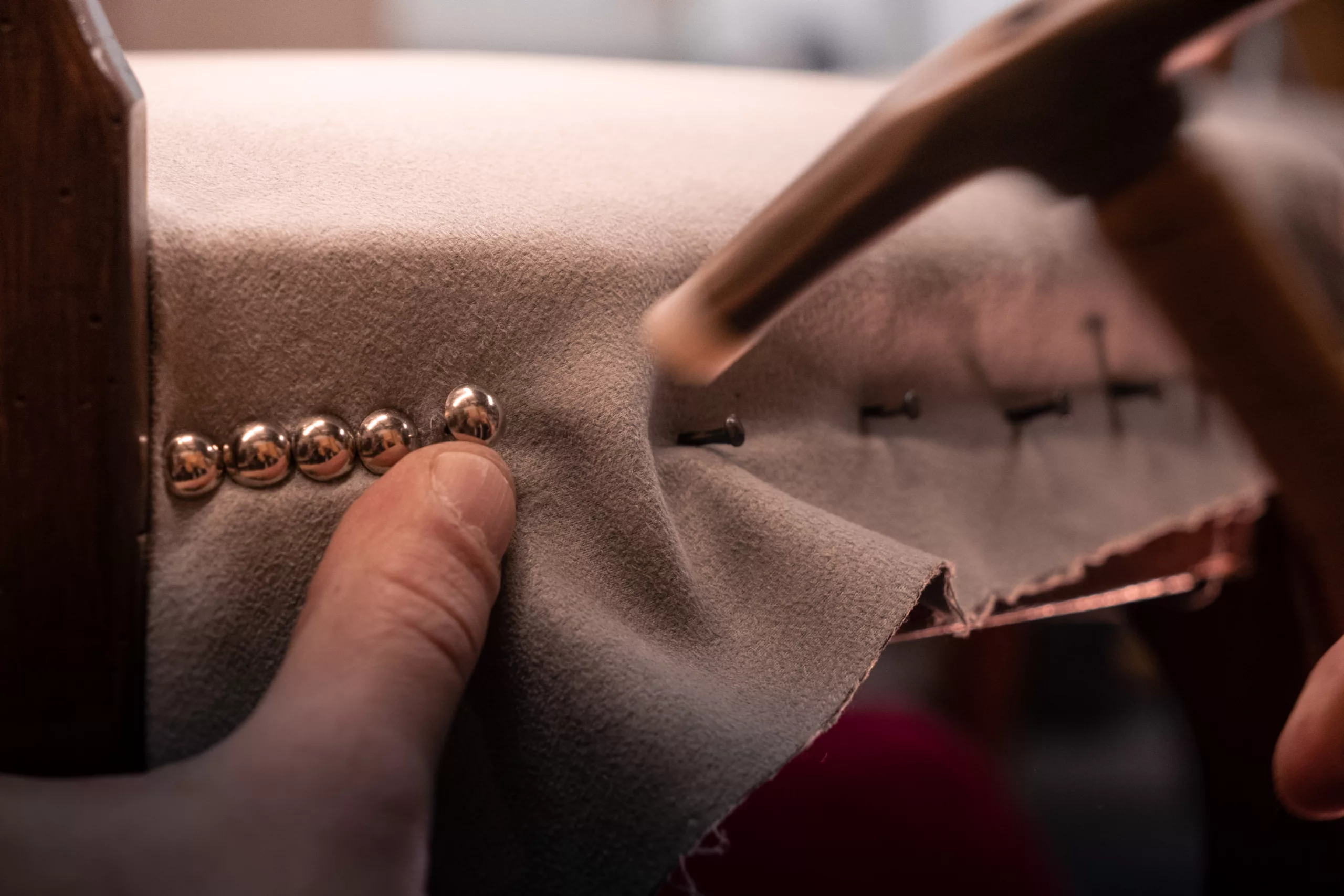travail à la main avec un ramponneau permettant d'insérer des clous décoratifs dorés sur une assise de siège de couleur beige