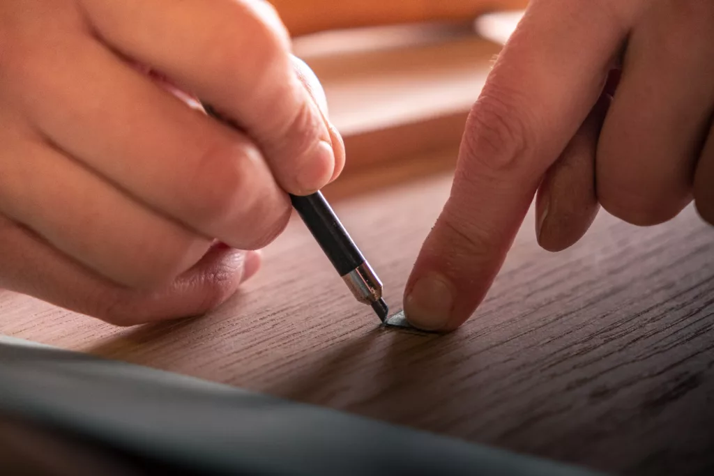main sur une pièce de bois réalisant un travail au crayon