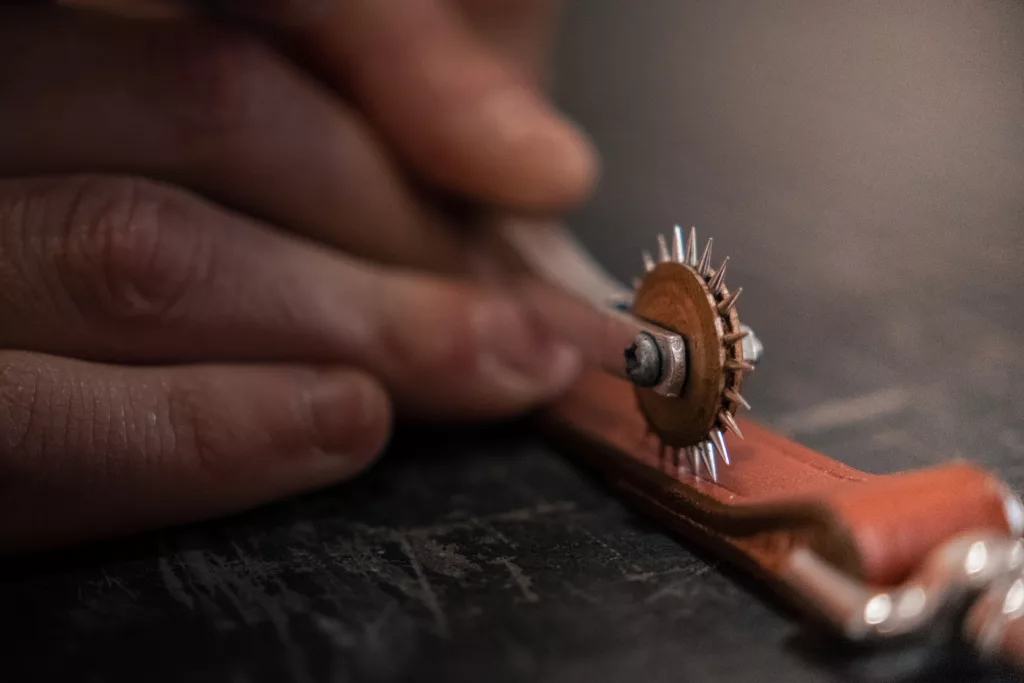travail à la main sur une pièce de cuir marron clair avec un outil type roulette dentelée